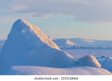 Winter Arctic Landscape. View Of Ice Hummocks, Frozen Sea, Coastline And Snow-capped Mountains. A Helicopter Flies In The Distance In The Sky. Shallow Depth Of Field. Chukotka, The Far North Of Russia