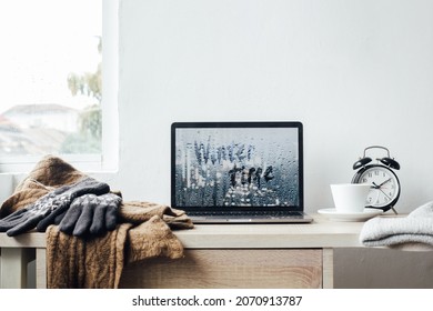 Winter background concept with winter time inscription on laptop screen with gloves and scarf on wooden table