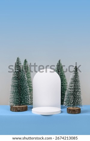 Winter background with cylindrical empty podium display for promotions and for showing product decorate. Stage pedestal or platform between Xmas trees on blue table. Merry Christmas celebration.