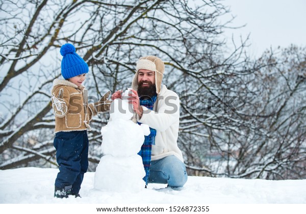 Winter background with snowflakes and\
snowman. Father and son making snowman in the snow. Handmade funny\
snow man. Best winter game for happy\
family