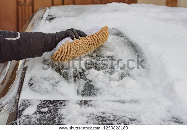 Winter bad weather, blizzard, a
man with a soft brush cleans the windows of the car from the
snow