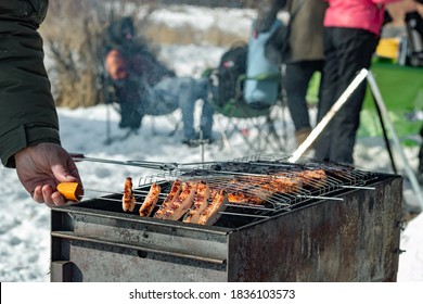 Winter barbecue outdoors, grill steak and fork with meat over hot coals, male hand cooking a BBQ at camping cookout