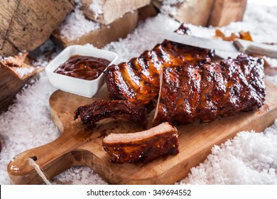 Winter barbecue with spicy marinated spare ribs on a wooden board outdoors in snow with a dipping sauce on the side
