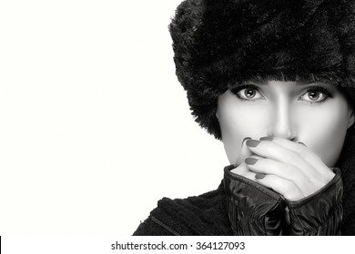 Winter beauty fashion girl with trendy fur hat and mittens warming her hands. Monochrome High fashion portrait isolated on white background with copy space for text