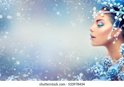 Winter Beauty Woman. Christmas Girl Makeup. Holiday Make-up. Snow Queen High Fashion Portrait over Blue Snow Background. Eyeshadows, False Eyelashes and Crystals on the Lips. Copy Space for Your Text 