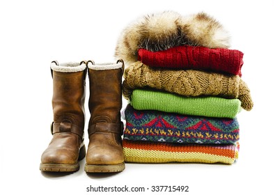 Winter boots, cap and stack of various sweaters. Winter style. Isolated on white background