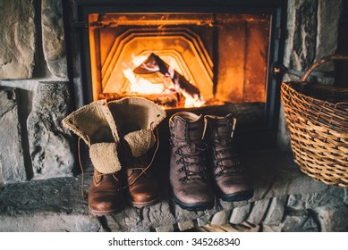 Winter Boots In Front Of A Fireplace. Family Vintage Folk Boots Drying Near The Fireside. Warm Cozy Fireplace In The Authentic Chalet. Hipster Shoes Getting Warm Near The Burning Fire In A Cabin. 