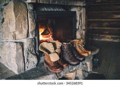 Winter boots in front of a fireplace. Family vintage folk boots drying near the fireside. Warm cozy fireplace in the authentic chalet. Hipster shoes getting warm near the burning fire in a cabin. 