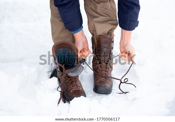 Winter boots put on\
by a man standing in the snow. Change shoes in winter shoes.\
Leather fur boots with\
lacing.