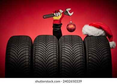 Winter car tires, big wheels, tyres, mechanic hand with wrench, christmas tree ball and Santa Claus hat on red background. - Powered by Shutterstock