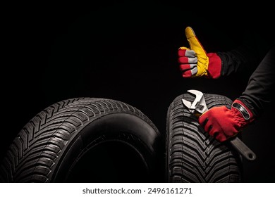 Winter car tires service and thumbs up hands of mechanic with wrench, screwdriver on black background. - Powered by Shutterstock