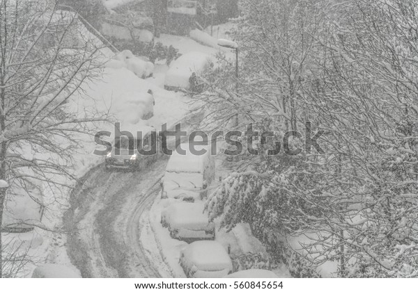 winter,\
cars driving on icy road covered with snow in a snowy day. winter\
background with street under snow during\
blizzard
