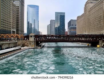 Winter in Chicago with elevated train passing over a frozen Chicago River covered in ice chunks. Path through ice was left after tugboat went through to break it up.