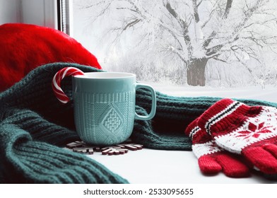 Winter Christmas background - cup with candy cane, woolen scarf and gloves on windowsill and winter scene outdoors. Christmas background with concept of spending winter holidays at cozy home - Powered by Shutterstock