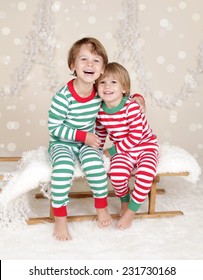 Winter Or Christmas Holidays: Laughing, Smiling, Happy Kids In Red And Green Striped Pj Pajamas On Wood Sled In Fake Snow, Snowflakes