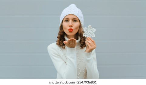 Winter christmas portrait of happy young woman blowing kiss with snowflakes decoration toys, red lipstick, on blue background, cheerful girl in white hat, sweater - Powered by Shutterstock