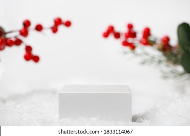 Winter Christmas scene with Ilex twigs on the background. Light white geometric pedestal for product presentation, cosmetics. Snow cube stand for advertising display