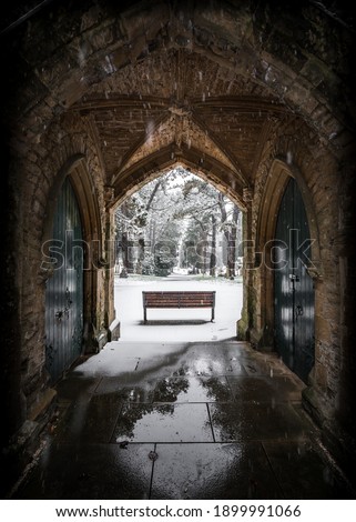 Winter churchyard grave yard with solitary bench in falling snow winter scene archway beautiful and peaceful blanket of snowfall Nottinghamshire cemetery local during pandemic lockdown 2021