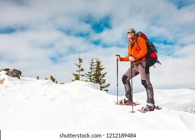 Winter Climbing The Mountain. A Man In Snowshoes Is Climbing To The Top. Winter Ascent. A Mountaineer With A Backpack And Trekking Sticks. Equipment For Winter Hiking.