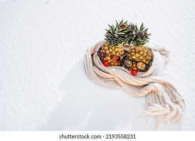 Winter is coming concept. Extreme cold winter weather with temperature below zero, climatic changes. Funny pineapple fruit men on snowy surface.