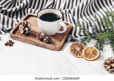 Winter composition. Breakfast in bed. Cup of coffee on wooden tray, wool blanket, fir tree branch, orange slices and pine cones. White linen table background. Festive cozy design. Selective focus. - Powered by Shutterstock