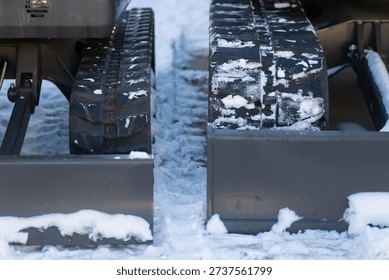 Winter construction teamwork with two excavators, contrasting tracks and skid plates shown in close up, snow and ice packed between machines