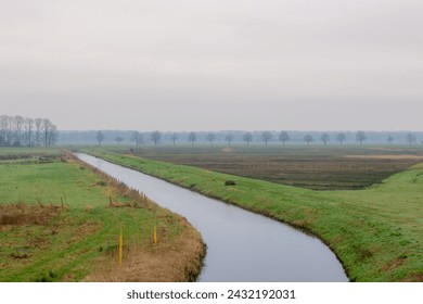 Winter countryside landscape, Typical Dutch polder with green meadow under cloudy sky and cold day, Flat and low land with small canal or ditch and the grass field, North Brabant province, Netherlands
