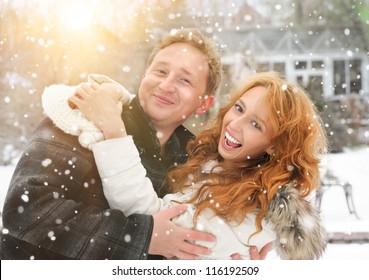 Winter Couple Piggyback In Snow Smiling Happy And Excited. Beautiful Young Couple At Backyard Of Their House