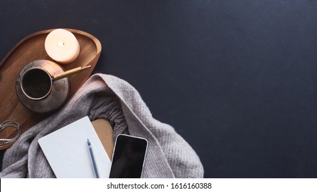 Winter Cozy Concept. Flatlay Of Gray Knitted Sweater, Candle, Coffee Drink, Diary, Phone, Glasses On Black  Table. Warm Weekend In Cold Weather. Dark Atmosphere