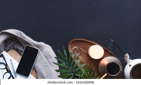 Winter Cozy Concept. Flatlay Of Gray Knitted Sweater, Candle, Coffee Drink, Diary, Phone, Glasses On Black  Table. Warm Weekend In Cold Weather. Dark Atmosphere