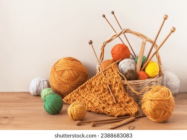 Winter crafts. Process of hand knitting warm bright scarf for cold season. Knitting supplies, set of colorful wool balls in wicker basket, wooden knitting needles and hooks on table. Knitting as hobby