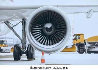 Winter day at airport during snowfall. Snowy jet engine of airplane. Snowplows clearing snow from runway.
 - Powered by Shutterstock