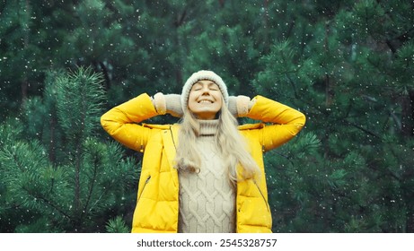 Winter day, happy woman enjoys snow, warm weather against Christmas tree, joyful girl in hat, yellow jacket in snowy green forest with snowflakes - Powered by Shutterstock