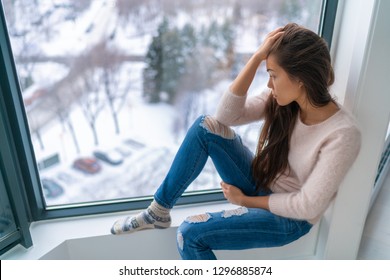 Winter depressed sad girl lonely by home window looking at cold weather upset unhappy. Bad feelings stress, anxiety, grief, emotions. Asian woman portrait. - Shutterstock ID 1296885874