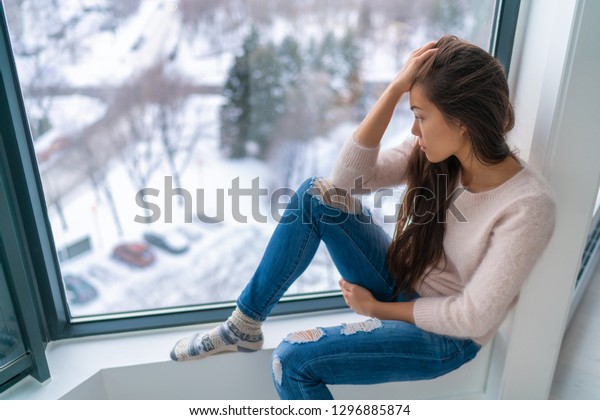 寒い天気を見つめながら 家の窓からさびしい寂しい悲しい女の子は 冬の憂鬱な女の子を悲しませた 悪い感情は ストレス 不安 悲しみ 感情を持つ アジアの女性のポートレート の写真素材 今すぐ編集
