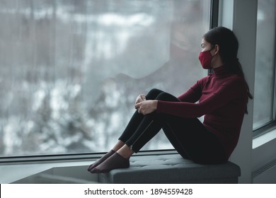 Winter Depression Because Of Coronavirus Confinement. Sad Asian Woman Alone During City Lockdown Wearing Face Mask Indoors At Home Covid. Anxiety, Stress, Mental Health Issues.