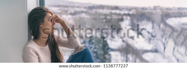 Winter depression sad\
woman with Seasonal affective disorder girl grief stricken alone at\
home window thinking negative thoughts. Mental health banner\
panorama background.