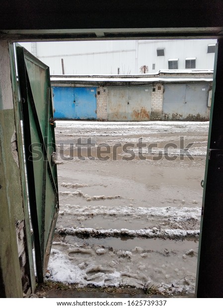 Winter dirty broken\
road in a garage cooperative. Gray depressing moody winter. Dnipro\
/ Ukraine - 12.13.2019