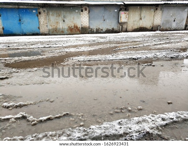 Winter dirty broken\
road in a garage cooperative. Gray depressing moody winter. Dnipro\
/ Ukraine - 12.13.2019
