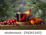 Winter drink with spices, cranberries, and citrus fruits on a background of green fir tree branches.