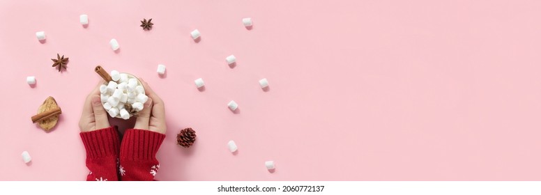 Winter drink, white mug with marshmallows in female hands in knitted Christmas Sweater on pink background. Top view, Flat Lay. New Year, Christmas traditional food. Festive decor, celebration Xmas
