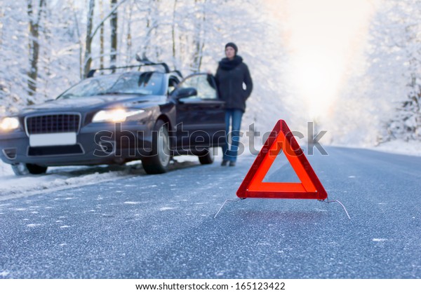 Winter driving - car breakdown Car breakdown on a\
country road in winter. Woman standing beside her car and waiting\
for help.