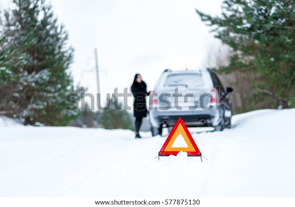Winter driving - car\
breakdown Car breakdown on a country road in winter. Woman standing\
beside her car