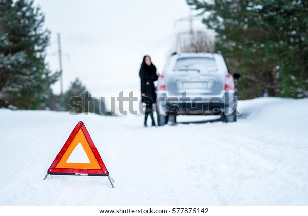 Winter driving - car\
breakdown Car breakdown on a country road in winter. Woman standing\
beside her car