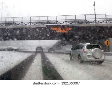 Winter Driving on Highway with Falling Snow on Windshield Passing Under a Bridge with an Electronic Winter Storm Warning Sign