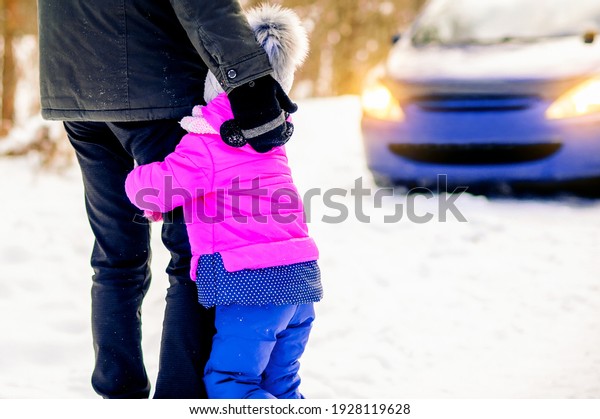 Winter Driving Road Safety, Safe Driving Tips for\
Winter Conditions. Little girl hugs dads leg on the background of\
car in winter day.