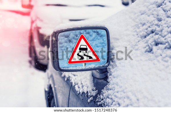 Winter driving - warning sign\
- slippery road. Winter driving - caution.  Concept of snow in the\
road. Car hit a snowstorm. Reflection of a road sign in a car\
mirror.