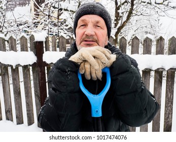 Winter. An Elderly Man Leans On A Snow Shovel