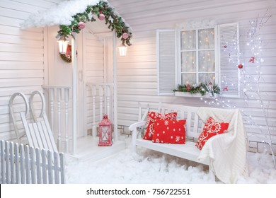 Winter Exterior Of A Country House With Christmas Decorations In The American Style. Snow-covered Courtyard With A Porch, Tree, White Bench And Wooden Vintage Sleds.