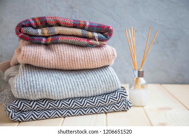 Winter and fall cozy sweaters stack, woolen sweaters and blankets still life with air freshener